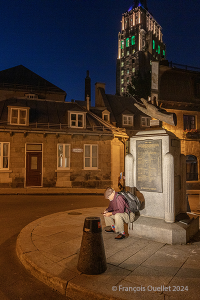 Un piéton se repose en soirée dans le Vieux-Québec, avec l'édifice Price en arrière-plan.